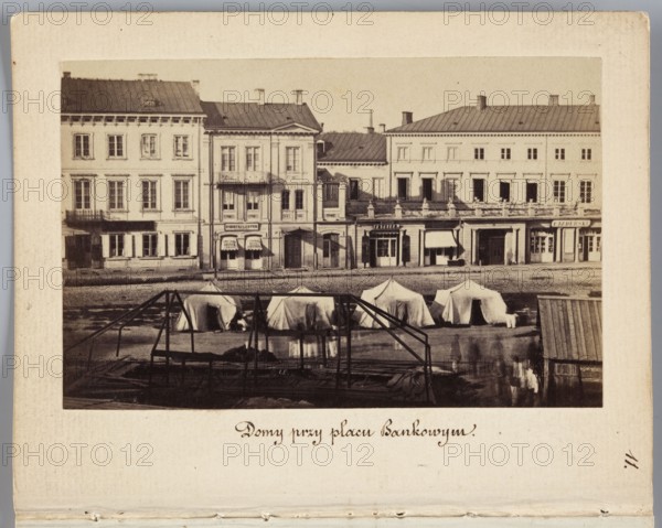 Houses at Bankowy Square Eastern frontage of Rymarska Street with Aleksander Przezdziecki's palace and a fragment of the Meynders tenement house, photograph by Karol Beyer 1818–1877; depicts tenement houses, Meynders' tenement house Rymarska 6, Aleksander Przezdziecki 1814–1871 and his palace, military tents and signs of the Russian army during martial law in the Kingdom of Poland 1861–1863; related iconography: Lessel/Fryderyk Albert 1767–1822, Podczaszynski/Boleslaw 1822–1876; photographer Leopold Méyet 1850–1912 noted; dated 1861–1863; photography, nature photography; photographic print: 6.2 × 9.6 cm; support: 11.3 × 8.8 cm., A sepia-toned photograph shows a row of older multi-story buildings with rectangular windows and pitched roofs, with a street-level arcade and awnings along the ground floor; in front of the buildings on an open area by the water there is a group of light-colored canvas tents and a few darker structures, and in the foreground a dark metal framework and wooden p...