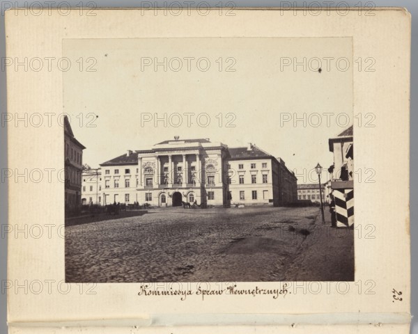 Mostowski Palace rebuilt to the design of architect Antonio Corazzi for the Government Commission of Internal Affairs and Police; view shows the exit of Nowolipie Street onto Przejazd Street at left and buildings of Nowolipki Street in the background at right. Photographer: Karol Beyer 1818–1877. Date: 1861–1863. Materials/format: photographic print, nature photography; image: height 6.8 cm, width 8.2 cm; support: height 11.3 cm, width 8.8 cm. Inscriptions/subjects: cobblestones, street lamps., A wide exterior scene showing a large classical building centered in the image with a grand façade featuring columns and decorative reliefs, flanked by lower buildings on either side; in front of the building is a broad cobblestone square with a few indistinct figures and horse-drawn carriages near the entrance, and a group of smaller structures and a striped guardhouse or booth at the right edge; the foreground shows textured cobbles and a slightly raised curb, and a tall street lamp stands nea...