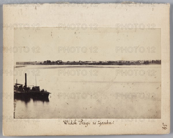 View of Praga from Zjazd View from Nowy Zjazd on the Praga bank of the Vistula, Beyer, Karol 1818–1877 author, Méyet, Leopold 1850–1912 photographer, 1860, Warsaw; subject: Vistula River and Praga district; photography, nature photography; photographic print: 6.2 × 9.5 cm; support: 11.4 × 8.8 cm., A sepia-toned photograph showing a wide, calm body of water filling most of the frame with smooth reflections near the bottom left where a dark silhouette of a docked boat or barge is visible; the boat has a tall vertical smokestack and blocky superstructure. Along the distant horizon a low strip of land is visible with a group of small structures and a few clusters of trees. The overall palette includes shades of beige, brown, cream, and dark brown to almost black in the boat silhouette, with subtle variations of off-white and tan in the sky and water.
