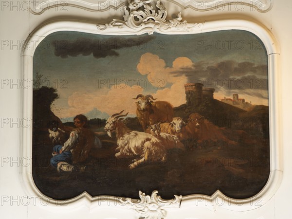 Shepherd Scene with a View of the Castle, Roos, Philipp Peter 1657–1706, painter. Multicolored composition with dominant shades of brown against a blue sky with white clouds and a distinct pink glow. In the foreground, the central group consists of two goats, a male and a female goat lying down, with a male goat standing behind them. On the left, a slope, a dog, and a shepherd sitting in half-profile, wearing a brown sheepskin coat, blue trousers, a white shirt, and stockings. On the right, in the background on a hill, two cylindrical buildings with castle buildings behind them. 18th century, Italy; overdoor. Height 92.0 cm, width 115.0 cm., A painted scene framed by an ornate white decorative border shows a pastoral landscape with a group of goats and sheep resting on dark earth under a sky of muted blue and gray with soft peachy clouds; a seated figure wearing brown and blue clothing sits among the animals, and a few rocky hills and a stone tower-like structure appear in the backgrou...
