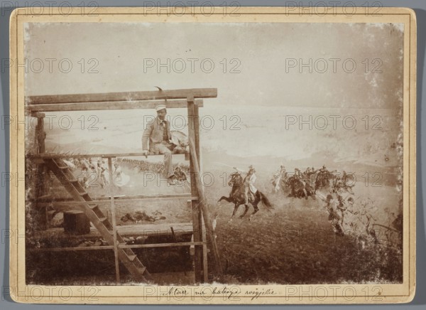 Painting the Raclawice Panorama: Wojciech Kossak with a palette on scaffolding next to a part of the canvas depicting Tadeusz Kosciuszko leading the second column of scythe-bearers into battle; painting, photographic print photography from nature, print glued onto cardboard backing; 1893/1894; photography: 11.9 × 17.12 cm, cardboard: 13.5 × 18.5 cm; Lviv; artists: Wojciech Kossak 1856–1942, Jan Styka 1858–1925; subject: Panorama of the Battle of Raclawice; iconography includes Tadeusz Kosciuszko 1746–1817, scythe-bearers, portraits of artists, painting accessories, scaffolding, palettes; painters' studio/panoramic painting work in progress., A sepia-toned image shows a wooden scaffold structure on the left with a man sitting on a horizontal beam; he wears a light-colored cap and clothes, and a bag rests beside him. The scaffold includes a slanted ladder and several horizontal and vertical beams. To the right, a group of mounted riders gallop across an open landscape, horses and riders ...