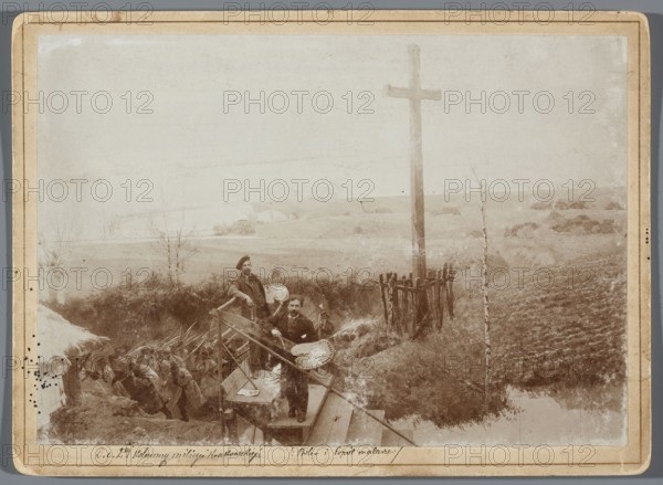 Painting the Raclawice Panorama: Tadeusz Popiel and Ludwig Boller standing with palettes on a scaffolding next to a part of the canvas depicting a cross at the Dziemierzyce crossroads; photograph by Hamel and Feigl, ca. 1892–1905. Reproduction of the Panorama of the Battle of Raclawice by Jan Styka and Wojciech Kossak; subjects include painters' studios, painting panoramas, painting accessories, portraits of artists, scaffolding, and palettes. Print glued to cardboard backing, photographic print 11.9 × 17.1 cm; cardboard 13.5 × 18.5 cm; 1893–1894; Lviv., The sepia-toned photograph shows an outdoor rural scene with a group of people gathered near a wooden structure and a tall wooden cross; the foreground includes a wooden stair or platform where a couple of men stand holding painter's palettes and brushes, one man leaning on the railing and another facing the camera; behind them a group of figures ascend a dirt slope carrying long objects that look like poles or rifles; the landscape be...