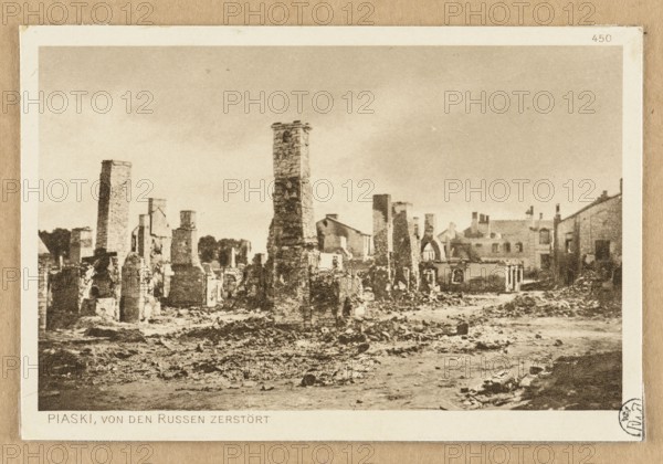 View of buildings destroyed by the Russians; postcard showing chimneys and war damage in a city view, glued across the entire surface to cardboard board. Photographer:, maker/publisher: JF Lehmanns Verlag Munich. Artist: Witke-Jezewski, Dominik 1862–1944. Date: circa 1914–1918. Postcard., The image shows a ruined landscape with a group of tall, damaged stone chimneys and broken masonry standing amid rubble and uneven ground; remnants of buildings and partial walls extend across the middle and background, with a few intact rooflines visible; the sky is overcast and pale; visible colors include beige, brown, tan, sepia, gray, and off-white.