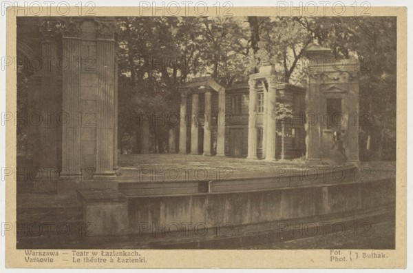 Warsaw. Theatre in Lazienki Park, Jan Bulhak 1876–1950 photographer, St. Wojciech's Printing House and Bookstore Poznan publisher, Polish Society of Railway Bookstores Ruch, Sp. Akc. Warsaw, Poznanska 38 publisher, ca. 1935, postcard, height 9 cm, width 14 cm, The image shows an outdoor scene of a stone stage or platform with classical architectural elements, including a row of tall fluted columns and several rectangular stone structures with pilasters and pediments, set against a backdrop of trees with visible foliage. The foreground includes a low stone wall or balustrade and a broad flat surface that appears worn, all rendered in sepia tones of brown, tan, and beige, with darker brown shadows and lighter beige highlights.