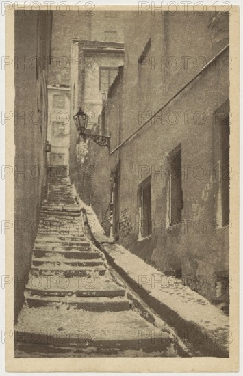 Warsaw. Old Town - Stone Stairs, St. Adalbert's Printing and Bookstore; Polish Society of Railway Bookstores Ruch publisher; Bulhak, Jan 1876–1950, photographer; ca. 1930; Stone Stairs, Warsaw street, Warsaw Old Town; postcard; 14 cm × 9 cm., A narrow, steep alleyway with worn stone steps leading upward between tall buildings, showing a rough stone path and a sloped gutter alongside the steps; the right building has several recessed windows and a textured, weathered wall, while the left side shows vertical building faces and a distant facade at the top of the alley; a decorative metal lantern extends from the left side near the middle of the scene. The image appears in muted tones of brown, beige, and sepia.