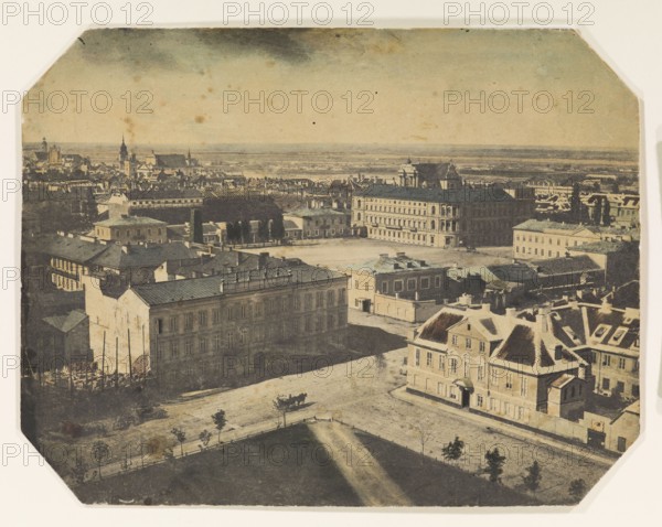 View from the lantern of the Holy Trinity Evangelical Lutheran Church towards Saxon Square now Józef Pilsudski Square, Warsaw. Photographer: Karol Beyer 1818–1877. Colored positive photograph, 1858. Shows city panorama including Saxon Square, Hotel Europejski, and Królewska Street. Paper corners cut diagonally. Photographic print on paper, 18.8 × 24.5 cm., Aerial view of an urban area showing a group of multi-story buildings with pitched and flat roofs in shades of beige, brown, tan, and muted gray, with a few darker slate-colored roofs; a large open square or courtyard between the buildings with shadows casting across it; a tree-lined promenade or park area with a row of small trees and a pathway in greenish and brown tones in the foreground; a horse-drawn carriage with dark figures and a dark animal on a pale street; clusters of rooftops and distant church spires and towers on the horizon in pale beige and gray; a sky with a gradient of pale cream to muted bluish-gray and some darker...