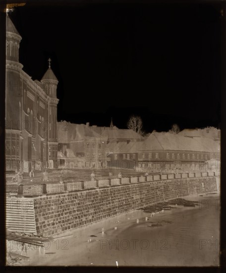 Vilnius. View from Užupis - Vilnia, fragment of Metropolitan and St. Anne Streets, side elevation of the Cathedral of the Most Pure Mother of God, Czechowicz, Józef 1818–1888 photographer, Vilnius Lithuania, architecture, Polish architecture, cathedrals, rivers, sacred architecture, Vilnia Lithuania, Belarus; river, Cathedral of the Most Pure Mother of God Vilnius, the upper part of the negative in the sky part sealed with black paper on the glass side; on the emulsion side retouched with black ink in the central part, 1880, Vilnius, negative, photograph, photograph from nature, height 30.2 cm, width 25.3 cm, A negative photographic image showing a riverbank with a stone retaining wall and a walkway above it, a group of buildings with pitched roofs behind the wall, and a large multi-towered building on the left; several human figures stand along the walkway; leafless trees rise above the rooftops; floating debris and wooden posts appear in the water; visible colors include shades of bl...