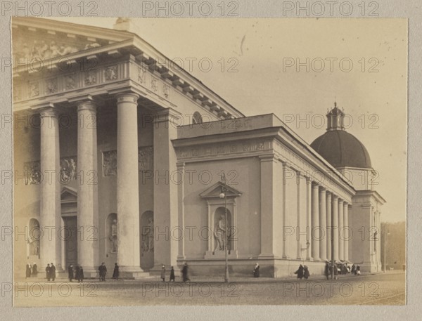 Vilnius. Cathedral Portal; photograph in the album Vilnius Temples, volume 1; Bulhak, Jan 1876–1950, photographer; Vilnius cathedral; pictorialism; photography, 1912; photograph, photographic print: 11.5 × 15.7 cm also listed 11.5 × 15.5 cm; backing: 31 × 22.5 cm; album page: 31.1 × 23.5 cm., A large classical building with tall columns and a pediment occupies most of the image, showing smooth round pillars in front and along the side, sculpted reliefs and niche statues set into the façade, and a domed roof toward the right; a group of people in dark clothing stand and walk near the base of the building, and there are street lamps and a lamppost visible along the sidewalk; the scene is rendered in sepia tones with shades of brown, beige, cream, and muted gray.