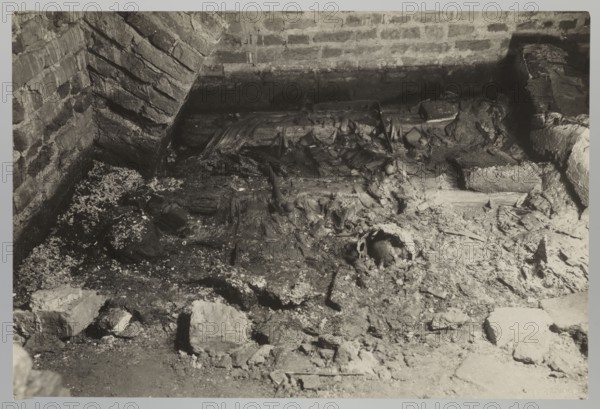 Vilnius. Cathedral - interior of the royal crypt, Bulhak, Jan 1876-1950, Vilnius Lithuania, Archcathedral Basilica of St. Stanislaus and St. Ladislaus, crypts, archaeological excavations, flood in Vilnius in 1931, 1931, photograph, photograph from nature, height 11.5 cm, width 16.5 cm, A close-up view of a rough, enclosed area with brick walls and a dirt floor showing debris and broken materials; the scene includes a brick corner with angled mortar lines, scattered chunks of masonry and rubble, splintered wooden planks and fragments, and areas of crumbly, uneven ground with dust and small granular particles. The visible colors are shades of black, white, and gray.