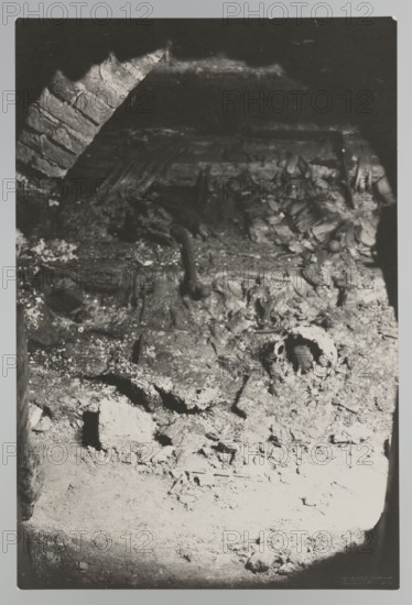 Vilnius. Cathedral - interior of the royal crypt; crypts; archaeological excavations after the 1931 flood in Vilnius; 1931; photographer Jan Bulhak 1876–1950; Archcathedral Basilica of St. Stanislaus and St. Ladislaus, Vilnius; photograph, gelatin silver natural photography; 16.7 × 11.5 cm., The image shows a dimly lit interior scene with a rough, uneven surface covered in debris and fragments, including a partially visible skull-like object among the rubble; a curved brick arch is visible in the upper left, and a few irregular shapes and broken pieces are scattered across the ground; colors visible are shades of black, white, and gray.