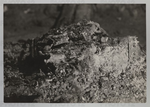 Vilnius. Cathedral — interior of the royal crypt, archaeological excavations; Barbara Radziwillówna Queen of Poland; 1520–1551; flood in Vilnius in 1931; 1931; Vilnius; photograph from nature; photograph; height 11.5 cm; width 16.8 cm, A close-up monochrome scene showing a textured mound of crumbled, rough material with chunks and fragments piled together, featuring irregular, granular surfaces and layered pieces. The image contains areas of light and deep shadow creating strong contrast across the uneven forms. Visible among the debris are a few angular, plate-like fragments and a group of rounded, pebble-like bits. Toward one side there is a partially exposed cylindrical object with a series of small rounded perforations along its edge. The overall colors visible are shades of black, white, and gray.