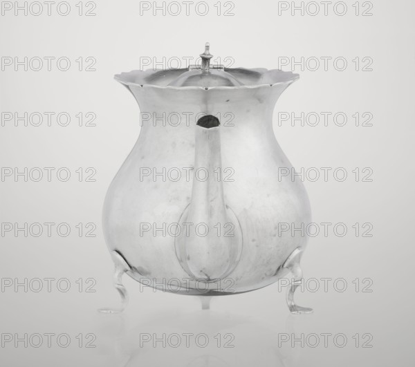 Pear-shaped teapot supported on three legs, smooth, with a flared upper edge topped with a pinnacle, with a spout-shaped spout, on the axis silver bushings for mounting the missing wooden handle. Maker: Stokes & Ireland Ltd Birmingham; goldsmiths; fl. 1872–1925. Inscription/markings: role classification of maker, goldsmiths. Date: 1900/1901. Place of origin: Chester, England, Great Britain. Material/function: vessel tea accessory. Dimensions: height 11.5 cm; width 15.5 cm; depth 10 cm; weight 330 g. Provenance: scrap - purchase, A metallic teapot-like vessel with a bulbous body and a wavy, scalloped rim sits on a smooth surface, shown from the front with a short, rounded spout protruding toward the viewer and a domed lid topped by a small finial; the vessel stands on a group of curved feet and displays a reflective, slightly worn surface in shades of silver and gray against a pale gray background.