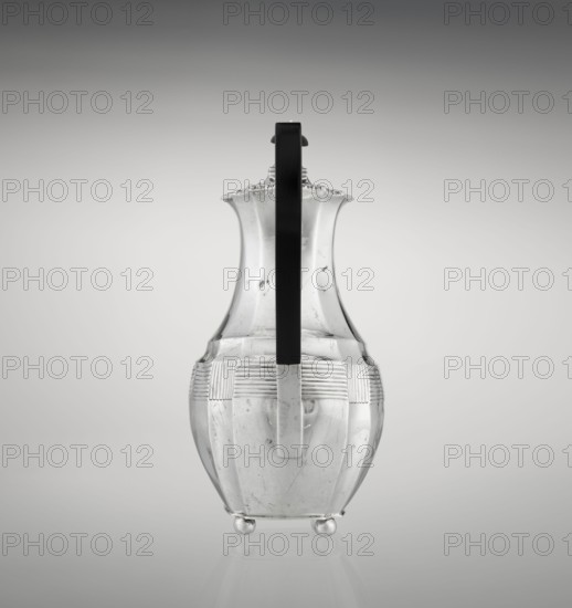 Coffee pot by Harris, CS & Sons London; goldsmiths' firm, fl. 1817–1933 and Charles Stuart Harris fl. 1852–1897 — purchased provenance, scrap - purchased. Pear-shaped, ribbed coffee vessel with godron ornaments; supported on four profiled, ball-shaped legs. Belly decorated with a band of narrow half-cylinders and grooves. High spout-like side handle and a wooden axial handle contemporarily added set in silver sockets. Upper edge edged with godron band; hinged lid domed in the center, topped with a bowling-pin finial. 1895/1896. Great Britain, London, England. Height 21.2 cm; width 18.5 cm; depth 10 cm; weight 640 g., A clear glass pitcher with a bulbous lower body tapering to a flared, scalloped rim is shown against a smooth gray background; the pitcher has a vertical black handle attached along its front, a band of horizontal ribbed texture around its upper body, and it rests on a group of small rounded feet, with visible surface blemishes and reflections on the glass in shades of cle...