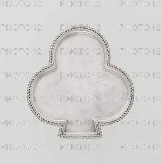 Tray, club-shaped with a smooth mirror surrounded by a raised half-cylinder edged with diagonal godron ornament. Maker: Hukin & Heath Birmingham; London; goldsmiths' firm; fl. 1855–1953; makers: John Thomas Heath and John Hartshorne Middleton. Date: 1897–1898. Place: London, England, Great Britain. Materials/subject: table accessory. Dimensions: height 1.1 cm; width 12.5 cm; depth 11.9 cm; weight 86 g. Provenance: purchase; scrap — purchase., A metallic tray shaped like a club with a raised decorative twisted rope border, showing a worn and slightly scratched surface; colors visible include silver, gray, off-white, and a pale background with subtle shadows.