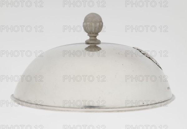Platter lampshade, Scott, Digby & Smith, Benjamin fl. 1802–1807 goldsmith; silver hemispherical lampshade with a non-original handle; smooth, with a ribbon edge, profiled; relief plaque with the Czartoryski coat of arms on a paludament, under a princely mitre, with labres and the motto Be that as it may.; handle is contemporary; 1803/1804; London, England, Great Britain; vessel; height 8.5 cm, diameter 15.2 cm, weight approx. 230 g, A dome-shaped metal cloche with a rounded finial handle on top, showing a smooth reflective surface with visible scratches and small blemishes; the cloche is primarily silver-gray with subtle darker gray areas and a few faint shadowed spots, and there is a decorative raised rim around the base and a small ornate element on one side.