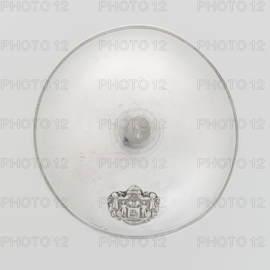 Platter lampshade, Scott, Digby & Smith, Benjamin fl. 1802–1807 goldsmith; silver hemispherical lampshade with a non-original handle, smooth, ribbon edge, profiled. On the side, a relief plaque with the Czartoryski coat of arms on a paludament, under a princely mitre, with labry and the motto Be that as it may. The handle is contemporary. 1803/1804, London, England; vessel; height 8.5 cm, diameter 15.2 cm, weight approx. 230 g., A circular metallic dish viewed from above with a smooth reflective surface showing scratches and faint scuff marks, a raised central knob, a decorative embossed crest near the rim, and a narrow rim around the edge; the visible colors are silver, gray, and subtle hints of off-white.