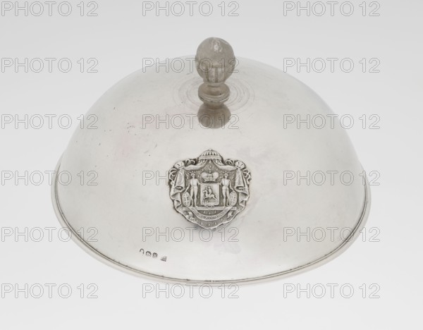 Platter lampshade, Scott, Digby & Smith, Benjamin fl. 1802–1807 goldsmith; silver hemispherical lampshade with a non-original handle, smooth, ribboned profiled edge; relief plaque with the Czartoryski coat of arms on a paludament, under a princely mitre, with labres and the motto Be that as it may.; handle is contemporary. 1803/1804; London, England, Great Britain. Vessel; height 8.5 cm, diameter 15.2 cm, weight approx. 230 g., A domed, reflective metallic cover with a rounded handle on top and an ornate crest-like decorative medallion on the front, showing raised relief figures and ornamentation; the surface shows minor scratches and spots; the visible colors are silver, gray, and subtle off-white tones.