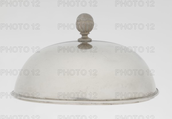 Platter lampshade, Scott, Digby & Smith, Benjamin fl. 1802–1807, goldsmith. Silver hemispherical lampshade with a non-original, contemporary handle; smooth surface with a profiled ribbon edge. On the side, a relief plaque with the Czartoryski coat of arms on a paludament, beneath a princely mitre, with labry and the motto Badz co sie Be that as it may. Dated 1803/1804, made in London, England, Great Britain. Vessel; height 8.5 cm, diameter 15.2 cm, weight approx. 230 g., A dome-shaped metal cloche with a rounded finial on top, showing a smooth curved surface with some small scratches and wear; the cloche and finial are metallic grey and silver, with slight darker patina on the finial, and a thin raised rim around the base.