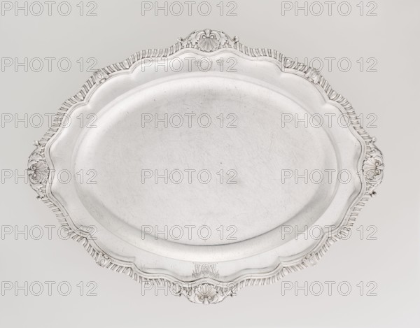 Oval Platter, Smith, Benjamin & James fl. 1809–1812 maker's role / goldsmith's firm; oval silver vessel, Georgian/George III style; smooth mirror with multi-leafed ribbed collar edged by a godron band with four shells on the axes, enclosed within acanthus leaves; engraved coats of arms on the shorter axis of the collar; underside of collar engraved monogram GvR, dated 1811/1812; England, London; height 3 cm, width 47 cm, depth 37.5 cm, weight 2420 g., A large oval metal tray with a smooth, slightly scratched central surface and a decorative scalloped rim featuring ornate shell and scroll motifs; the tray and its details appear in shades of silver and light gray against a pale off-white background.