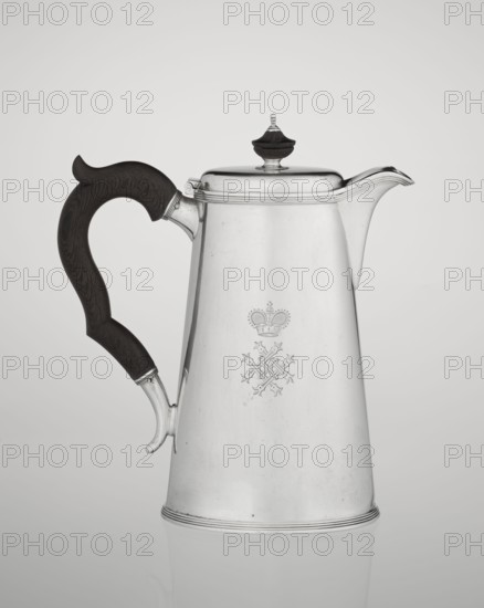 Conical coffee pot with hinged lid, slightly arched and flattened at the top, topped with a wooden handle made; short spout on the axis with two sleeves for attaching a wooden handle added contemporarily. Mantle engraved with monogram tied HH under a ducal mitre and dated 1890/1891. Maker: Barnard, Edward & Sons Ltd London; goldsmiths, fl. ca. 1680– ; later associated with Clark, Alfred Ltd London; goldsmiths and sellers, fl. 1898–1934. Materials: silver and wood. Subject/function: coffee ware. Place: London, England, Great Britain. Dimensions: height 17.3 cm, width 11 cm, depth 8.4 cm; weight 627 g., A tall metal pitcher with a conical body and polished silver surface stands against a neutral light gray background, featuring a curved wooden handle in dark brown with visible grain attached to one side and a short metal spout on the opposite side, a hinged lid topped with a small dark brown finial, a faint decorative emblem engraved on the front of the body, subtle concentric ridges nea...