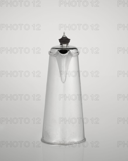 Coffee pot by Barnard, Edward & Sons Ltd London; goldsmith's firm; fl. ca. 1680–, with later association to Clark, Alfred Ltd London; goldsmith's firm and sellers; fl. 1898–1934. Conical coffee pot with hinged lid, slightly arched and flattened at the top, topped with a wooden handle; short spout; on the axis two sleeves for attaching a wooden handle added contemporarily. On the mantle engraved monogram tied HH beneath a ducal mitre; dated 1890/1891. Material: silver with wooden handle. Place: London, England, Great Britain. Function: coffee ware. Dimensions: height 17.3 cm, width 11 cm, depth 8.4 cm; weight 627 g., The image shows a tall, tapered metal pitcher with a rounded lid topped by a dark finial; the pitcher has a smooth, reflective surface with subtle scratches and a small spout near the top, and it sits against a plain light gray background with a faint reflection beneath. The visible colors are silver, dark brown or black on the finial, and shades of light gray in the backgr...