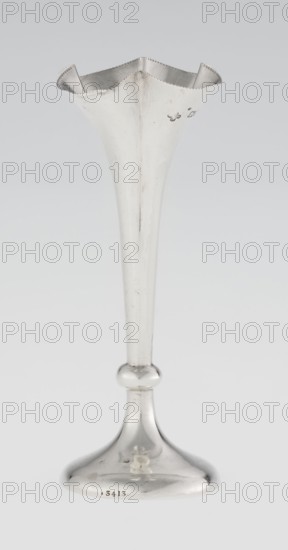Chalice-shaped vase, maker: Woodward, Horace & Co Ltd Birmingham, London; fl. ca. 1851–1919. Goblet-style vessel in the form of a slender flower calyx: supported on a circular foot, transitioning into a short stem terminating in a ring; tall conical body with a quarter-part at the top, edged with pearling. Ornament: pearling; motif: flowers. Date: 1899–1900. Place: Great Britain — England, London. Material/type: vessel. Dimensions: height 12.5 cm; width 5.5 cm; depth 5.5 cm; weight 38 g., A tall metallic vase-like object with a flared, scalloped rim and a long tapered stem rising from a rounded base, all in silver tones with reflective highlights and some darker tarnished areas; the surface shows a few small scratches and marks, and the background is a smooth light gray.