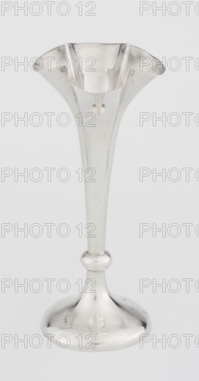 Chalice-shaped vase by Woodward, Horace & Co Ltd Birmingham, London; fl. ca. 1851–1919. Maker's role/corporate slogans/goldsmith's firm. Purchase provenance. Scrap - purchase. Flowers vessel; pearling ornament. Vase supported on a circular foot transitioning into a short stem terminating in a ring, with a goblet in the form of a slender flower calyx; tall, conical, quarter-part at the top, edged with pearling. 1899–1900. Great Britain, England, London. Vessel. Height 12.5 cm; width 5.5 cm; depth 5.5 cm; weight 38 g., A single tall metallic vase with a flared, scalloped rim and a long tapered stem ending in a rounded base, finished in a reflective silver color with subtle surface marks and highlights, placed against a plain light gray background.