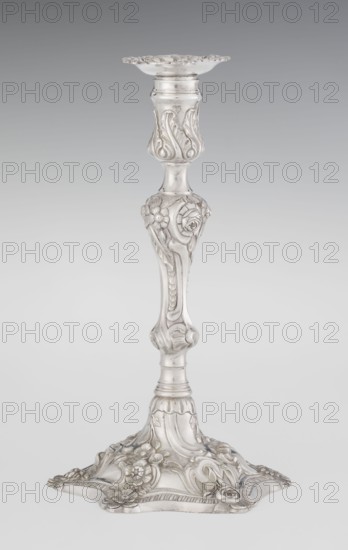 Single-candle candlestick by William Cafe fl. 1757–ca.1802, 1763/1764. Rococo, George II style; silver lighting fixture on a raised, domed foot with a hexagonal rim decorated with flower heads at the corners, passing into a baluster shaft and terminating in a vase-shaped socket with a disc-shaped drip pan. Decorated in rocaille motifs—plant tendrils, flowers, cartouches, shells and acanthus leaves—with a slight spiral twist to the overall decoration. England, London. Height 29 cm; diameter 16.9 cm; weight 695 g., A single ornate candlestick stands against a smooth gradient background; it is metallic silver in color with polished and slightly matte areas, featuring a decorative flared top, a slim shaft with curving contours, a bulbous section adorned with floral and leaf reliefs, and a wide ornate base with raised floral motifs and scrolling designs.