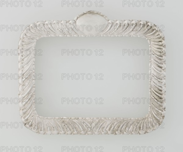 Dressing mirror frame, Comyns & Sons London; goldsmiths; fl. 1859–1953 maker; scrap; clasp; medallion; rectangular mirror frame with rounded corners decorated with oblique clasp and oval medallion; 1890/1891; Great Britain, England, London; dressing accessory; frame; height 15.7 cm; width 13.2 cm; depth 2 cm; weight 102 g., A decorative rectangular frame with rounded corners and an ornate raised pattern, shown against a pale background; the frame appears metallic with shades of silver and off-white, and contains a smooth oval cartouche at the top center.