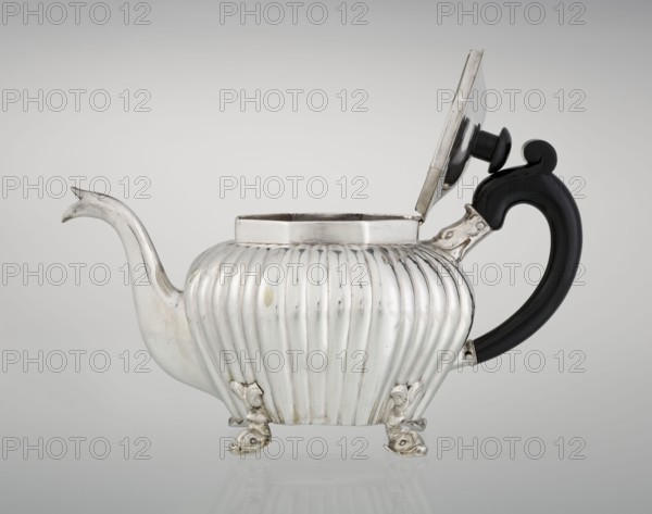 Teapot, maker Thomas II fl. 1798–1809?, goldsmith. Teapot supported on four legs in the form of dolphins, octagonal, decorated with vertical narrow ringlets and flutes, with a spout-shaped spout, with a wooden handle not original mounted in sockets, with a slightly arched hinged lid, wooden finial/handle not original. Iconography: dolphin; function: tea vessel. Date: 1808–1809. Place: London, England, Great Britain. Materials: silver implied by goldsmith and wood handle. Dimensions: height 12 cm, width 20.5 cm, depth 14 cm; weight 595 g. Provenance note: scrap - purchase; purchase., A silver teapot with a fluted, rounded body standing on a group of ornate feet, a curved spout on one side and a black curved handle on the other, the hinged lid is open showing the inner rim; visible colors include silver, black, and subtle reflections of gray.
