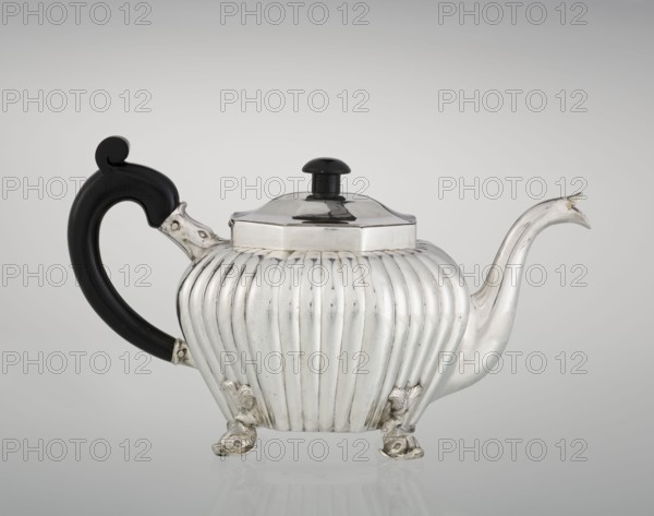 Teapot, Holland, Thomas II fl. 1798–1809? goldsmith, tea vessel. Teapot supported on four legs in the form of dolphins; octagonal; decorated with vertical narrow ringlets and flutes; spout-shaped spout; slightly arched hinged lid; wooden handle not original mounted in sockets. Dolphin iconography; ringing. 1808/1809. England, London. Vessel. Height 12 cm; width 20.5 cm; depth 14 cm; weight 595 g., A silver teapot with a ribbed, rounded body sits on ornate feet and has a curved, elongated spout and a high, domed lid topped with a small knob; the handle is black and curving with a decorative scroll at the top and connects to the body with silver mounts. The visible colors are silver, black, and subtle gray reflections.