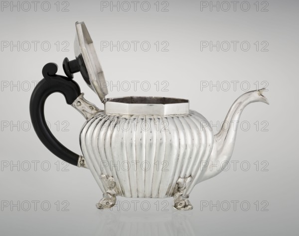 Teapot, maker Thomas II fl. 1798–1809?, goldsmith. Teapot supported on four legs in the form of dolphins; octagonal body decorated with vertical narrow ringlets and flutes; spout-shaped spout; slightly arched hinged lid with wooden handle not original; additional wooden handle not original mounted in sockets. Iconography: dolphin; function: tea vessel. Date: 1808/1809. Place: London, England, Great Britain., silver scrap?, tea vessel. Dimensions: height 12 cm, width 20.5 cm, depth 14 cm; weight 595 g. Provenance: purchase., A silver teapot with a ribbed, rounded body sits on a reflective surface, its hinged lid open and revealing a dark interior; the teapot has a curved spout with a pointed tip and a black, curved handle attached with silver fittings, and it rests on decorative feet shaped like stylized animal forms. Colors visible include silver, black, dark gray, and pale gray in the background.