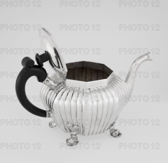 Teapot, Holland, Thomas II fl. 1798–1809? goldsmith, scrap - purchase, tea vessel, dolphin iconography, ringing, tea vessels. Teapot supported on four legs in the form of dolphins, octagonal, decorated with vertical narrow ringlets and flutes, with a spout-shaped spout, with a wooden handle not original mounted in sockets, with a slightly arched hinged lid, with a wooden handle not original. 1808/1809. England, London. Vessel. Height 12 cm; width 20.5 cm; depth 14 cm; weight 595 g., A metallic teapot with a ribbed, rounded body and a hinged lid is shown with the lid open, revealing a dark interior; the teapot has a curved spout and rests on a group of ornate feet, and it features a black, curved handle with a decorative knob at the top; visible colors include silver, black, and shades of gray.