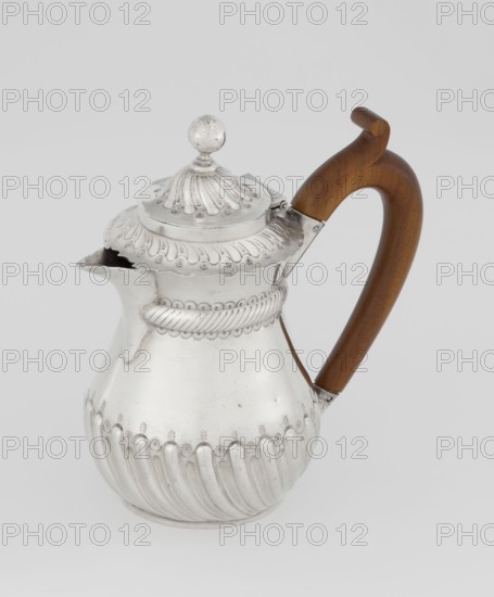 Coffee pot by John Septimus Beresford London; goldsmith's firm; active 1880–89. Pear-shaped jug, lower part spirally fluted, smooth above, decorated with a half-cylinder beneath the upper flared rim; short spout, wooden handle mounted in sleeves not original, hinged domed lid, spirally knotted, topped with a ball. 1888–1889. Great Britain — England, London. Vessel. Height 13 cm, width 12 cm, depth 6.8 cm, weight 179 g., A silver pitcher with ornate embossed patterns and a rounded ribbed lower body sits against a light gray background, topped by a domed lid with a round finial and decorative scalloped edges, and featuring a curved wooden handle in brown attached to the metal body; visible colors include silver, brown, and light gray.