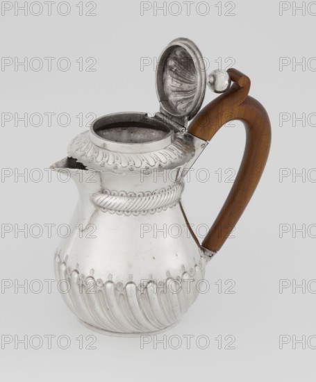 Coffee pot by John Septimus Beresford London; goldsmith; active 1880–1889. Pear-shaped jug, spirally clacked in the lower part and smooth above, decorated with a half-cylinder under the upper flared rim. Short spout, wooden handle mounted in sleeves not original, hinged domed lid, spirally knotted and topped with a ball. Dated 1888/1889. Great Britain — England, London. Vessel. Height 13 cm; width 12 cm; depth 6.8 cm; weight 179 g., A silver pitcher with decorative ridges and floral-like embossed patterns sits against a light gray background, its hinged lid open to reveal a textured interior; the spout is short and slightly flared, and a curved wooden handle in warm brown tones is attached to the pitcher with metal fittings.