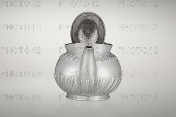 Teapot by Goldsmiths & Silversmiths Co Ltd London; makers William Gibson & John Langman goldsmiths. Egg-shaped tea vessel on an oval foot, decorated with two bands of diagonal clasp, with a high upper edge, hinged lid topped with a handle decorated with a wooden rosette, prominent spout, non-original wooden handle set in silver sockets. Made in modern times, 1896/1897, Sheffield, England. Dish. Height 13.5 cm, width 22.8 cm, depth 13.8 cm, weight 666 g., A reflective metal teapot with a rounded body and a hinged, open lid revealing the underside of the lid, finished in silvery gray tones with a few darker gray areas inside the lid and on the spout, featuring raised decorative ridges around the upper and lower portions, a central spout extending from the front, and a short circular base, all set against a smooth pale gray to off-white gradient background.