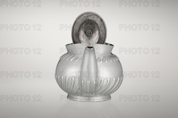 Teapot, made by Goldsmiths & Silversmiths Co Ltd London; makers William Gibson & John Langman goldsmiths. Egg-shaped teapot on an oval foot, decorated with two bands of diagonal clasp, with a high upper edge, hinged lid topped with a handle decorated with a wooden rosette, prominent spout on the side, non-original wooden handle set in silver sockets. Tea vessel tea accessory. Made 1896/1897, Sheffield, England. Dish. Height 13.5 cm, width 22.8 cm, depth 13.8 cm, weight 666 g., A metallic teapot with a rounded body and an open hinged lid is centered against a light gray background, showing a smooth reflective surface with decorative vertical ridges around its lower and upper halves, a short rounded spout at the front, and a slightly raised circular base; the visible colors are silver, gray, and subtle darker gray tones inside the lid.