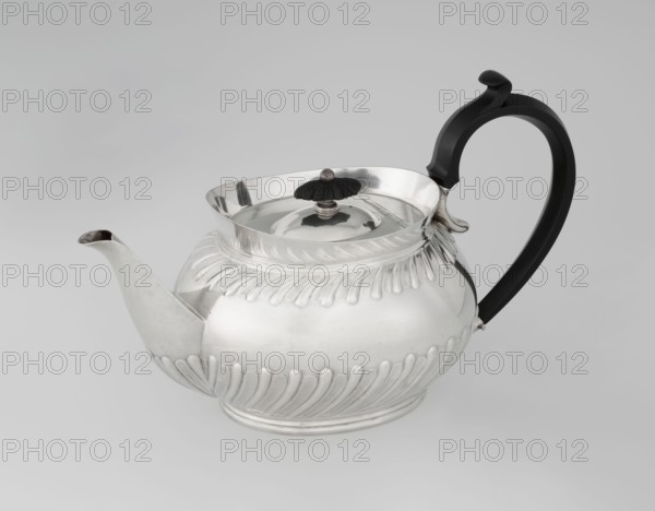 Teapot by Goldsmiths & Silversmiths Co Ltd London; makers William Gibson & John Langman goldsmiths. Egg-shaped silver teapot on an oval foot, decorated with two diagonal bands, high upper edge, hinged lid topped with a wooden rosette, prominent spout on the side, non-original wooden handle set in silver sockets. Maker's mark dates 1896–1897. Modern additions noted. Height 13.5 cm; width 22.8 cm; depth 13.8 cm; weight 666 g. Made in Sheffield, England., A polished metal teapot with a rounded, ribbed body and a fluted decorative band around its upper and lower sections sits on a neutral gray surface. The teapot is primarily silver in color with reflective highlights and subtle shadows, and it has a curved spout extending from one side. A dark black curved handle with a stylized top attaches to the opposite side, and a small dark finial rests atop the lid, which has a shallow open rim. The overall scene shows a clean, studio-lit setting with shades of gray in the background.