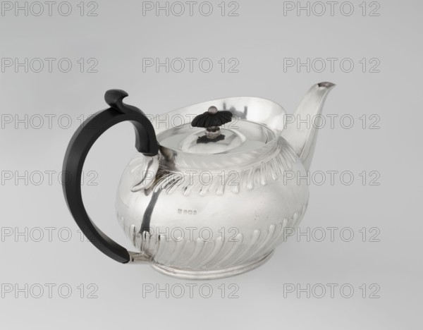 Teapot by Goldsmiths & Silversmiths Co Ltd London; makers William Gibson & John Langman goldsmiths. Egg-shaped silver teapot on an oval foot, decorated with two bands of diagonal clasping, with a high upper edge, hinged lid topped with a wooden rosette, prominent spout, non-original wooden handle set in silver sockets. Made in 1896/1897, Sheffield, England. Tea vessel; height 13.5 cm, width 22.8 cm, depth 13.8 cm, weight 666 g., A silver teapot with a rounded, ribbed body and a flared spout sits on a pale neutral background; it has a curved black handle attached at the top and bottom, a domed lid topped with a small dark finial shaped like a flower, and polished reflective surfaces showing highlights and subtle shadows in silver, black, gray, and white.