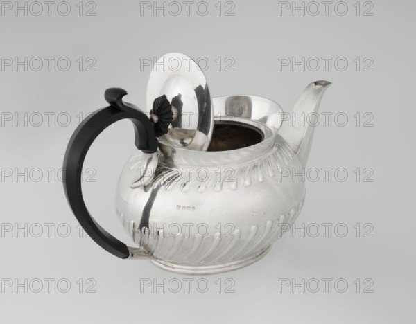 Teapot by the Goldsmiths & Silversmiths Co. Ltd London; goldsmiths' firm, fl. 1880–1952; makers William Gibson & John Langman goldsmiths. Egg-shaped tea vessel on an oval foot, decorated with two bands of diagonal clasp and a high upper edge; hinged lid topped with a handle decorated with a wooden rosette; prominent spout on the side; non-original wooden handle set in silver sockets. Made in modern times, 1896–1897, Sheffield, England. Materials: silver and wood. Dimensions: height 13.5 cm, width 22.8 cm, depth 13.8 cm; weight 666 g. Provenance: scrap — purchase, purchase., A shiny metal teapot with a rounded, ribbed body and a flared spout sits on a light gray surface against a pale gray background; the teapot has a hinged lid that is open, revealing a dark interior, and the lid features a small decorative knob with petal-like details; a curved black handle with a smooth finish attaches to the side opposite the spout, and there are reflective highlights and subtle surface scratches on...