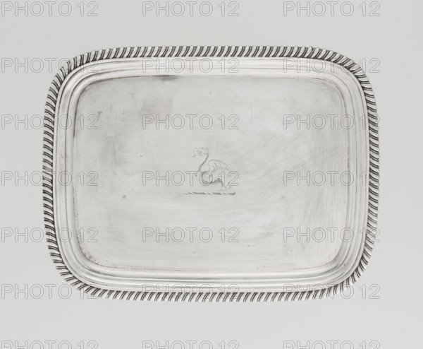 Tray on legs by William Bennet fl. 1796–1825, goldsmith. Tray on four legs in the form of stylised lotus flowers, rectangular with rounded edges, with a mirror; decorated with an engraved representation of a swan drawing heavily worn; raised, profiled collar; edge decorated with a godron ribbon. Godron ornaments; English Regency style; swans iconography. Date: 1811/1812. Maker location: London, England. Materials/technique: presumed silver, engraved. Dimensions: height 3.3 cm, width 26.6 cm, depth 20.4 cm; weight 758 g., A rectangular metal tray with rounded corners resting on a light gray background, the tray surface appears silver with visible circular and linear scratches and a few subtle darker smudges; a decorative twisted rope-like border runs along the edge in silver tones; the inner rim features a stepped profile also in silver; at the center of the tray a faint embossed or engraved emblem is visible in the same silver color.
