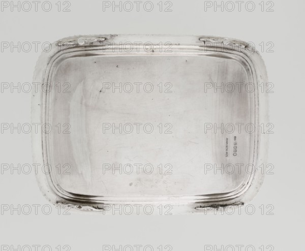 Tray on legs by William Bennet fl. 1796–1825, goldsmith. English Regency style, 1811/1812, London, England. Rectangular tray with rounded edges on four legs shaped as stylized lotus flowers, with a mirror and raised profiled collar. Edge decorated with a godron ribbon; surface engraved with a heavily worn representation of a swan. Height 3.3 cm, width 26.6 cm, depth 20.4 cm, weight 758 g., A rectangular metal tray with rounded corners sits against a neutral light gray background, showing a smooth flat interior surface with visible scuffs and scratches and a slightly darker patina in places; the tray has a raised stepped rim with a beaded outer edge and decorative raised handles integrated into the rim at opposite sides, and the visible colors are shades of silver and gray with subtle darker gray marks.