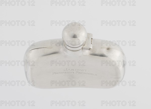 Hip Flask by James Dixon & Sons Sheffield; goldsmiths; active from 1806. Silver hip flask, smooth cuboid with rounded edges, narrow neck with spherical hinged stopper. Engraved on the bottle: JAN / TRUE FRIENDS. Date: 1925/1926. Place: Sheffield, England. Function: alcohol vessel. Dimensions: height 9.9 cm; width 9.6 cm; depth 2.6 cm; weight 110 g., A metallic flask with a rounded rectangular body and a domed screw cap attached by a small hinge sits against a pale background; the flask surface is reflective with visible scuffs, scratches, and slight dents, showing shades of silver, gray, and subtle darker tarnish marks.