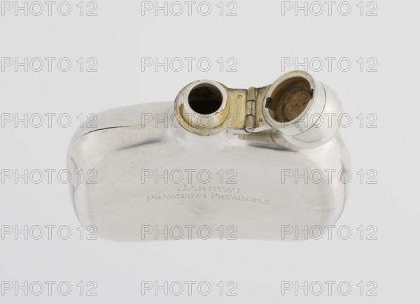 Hip flask by James Dixon & Sons Sheffield; goldsmiths; fl. 1806–, silver, smooth, cuboid with rounded edges, narrow neck with a spherical hinged stopper. Engraved JAN / TRUE FRIENDS. Alcohol vessel, 1925/1926. Sheffield, England. Height 9.9 cm; width 9.6 cm; depth 2.6 cm; weight 110 g., A smooth metallic object with a reflective silver surface rests against a pale gray background, showing a rounded rectangular body with gently curved edges and a hinged circular opening at one end that reveals an inner surface with a warm yellowish-brass tone; the exterior silver finish displays subtle scratches and faint darker marks, and there is a visible seam and slight dent along one side.