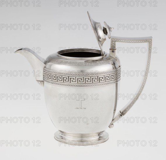 Teapot by John Emes fl. 1796–1808, goldsmith. Ovoid teapot on a circular base with lid, decorated on the upper belly with a wide band of meander ornament and braid. Side features a ribbon-shaped, broken handle decorated with braid; high-set spout decorated at the base with a stylised palmette; lid finished with a knob-shaped handle. Belly engraved with a coat of arms on one side and a cross on the other. Empire/Georgian/George III style, circa 1806–1807, London, England. Medium: silver vessel. Height 17.9 cm; width 23.7 cm; weight 815 g., A polished metallic jug with a reflective silver surface sits against a pale background, featuring a curved spout on one side and an angular handle on the other; the lid is open and attached by a hinge, showing a dark interior rim. The body of the jug has a decorative band near the top with a repeating geometric pattern and a subtle engraved border, and the lower body is smooth with a small simple engraved emblem. The handle and spout have matching de...