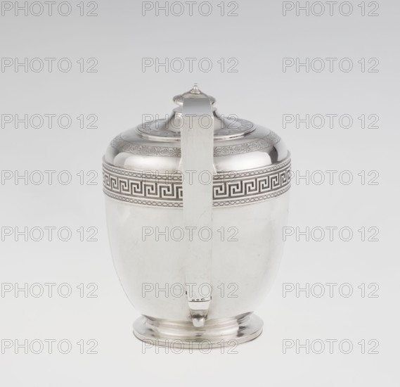 Teapot by John Emes fl. 1796–1808, 1806–1807, London, England. Ovoid teapot on a circular base with a lid; height 17.9 cm, width 23.7 cm, weight 815 g. Silver vessel in Georgian/George III Empire style. Upper belly decorated with a wide band of meander ornament and braid; side with a ribbon-shaped, broken handle decorated with braid. Spout set high, decorated at the base with a stylised palmette. Lid finished with a knob-shaped handle. Belly engraved with a coat of arms on one side and a cross on the other., A reflective metallic vessel with a rounded body and a domed lid topped by a small finial is shown against a plain light background, with a straight vertical handle running from the lid to the base; the vessel has an ornamental band around its upper portion featuring a repeating geometric fret pattern and additional decorative borders, and the visible colors are silver and shades of light gray.