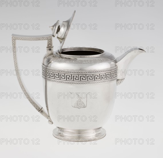Teapot by John Emes fl. 1796–1808, goldsmith. Ovoid teapot on a circular base with lid; upper part of the belly decorated with a wide band of meander ornament and braid. Side features a ribbon-shaped, broken handle decorated with braid. High-set spout with base ornamented by a stylised palmette. Lid finished with a knob-shaped handle. Belly engraved with a coat of arms on one side and a cross on the other. Styles: Empire, George III/Georgian. Inscription/marks: 1806/1807, London, England. Material: assumed metal vessel; height 17.9 cm, width 23.7 cm, weight 815 g., A silver metal pitcher with a hinged lid shown open, featuring a curved spout and a tall angular handle; the body is rounded with a short circular foot and decorative engraved bands around the upper portion and handle, and an engraved emblem on the front. Colors visible include silver and subtle darker gray tones from shadows and engraved details, against a light gray to white background.