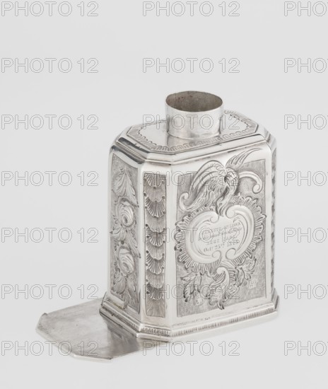 Tea caddy, Nash, Bowles fl. 1720–ca.1725 maker: goldsmith; rococo style; made for loose-leaf tea; cuboid tea caddy with a circular domed lid and a bowl on top; chamfered side edges; movable slide-in bottom. Surface decorated with repoussé floral and rocaille motifs on a grained background; front has an oval rocaille cartouche topped with an eagle containing an engraved inscription: KENNETH Mc LEOD, / to his much loved Sister / ANNE ZABA, / Octr 23 rd 1848; back wall with a bouquet of flowers; side walls with blooming leafy roses. Engraved A on the bottom. Dates: 1723/1724 tins; decoration ca. mid-19th century. Origin: London, England, Great Britain. Vessel. Height 12 cm, width 7.7 cm, depth 5.7 cm, weight ca. 230 g., The image shows a metallic, silver-colored ornate container with an open cylindrical neck on top and an attached flat base extension. The container has an octagonal form with decorative panels on its sides featuring embossed floral and foliate motifs, curved scrollwork, an...
