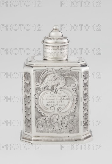 Tea caddy by Nash Bowles fl. 1720–ca. 1725, goldsmith. Rococo style; cuboid tea caddy with a circular domed lid and a bowl on the top; chamfered side edges; movable slide-in bottom. Surface decorated with repoussé floral and rocaille motifs on a grained background; front features an oval rocaille cartouche topped with an eagle containing an engraved inscription: KENNETH Mc LEOD, / to his much loved Sister / ANNE ZABA, / Oct 23rd 1848; back shows a bouquet of flowers; sides display blooming, leafy roses. Engraved S on the bottom. Dates: 1723/1724 tins; ca. mid-19th century decoration. Place of origin: London, England, Great Britain. Material/function: vessel for loose-leaf tea. Dimensions: height 12 cm, width 7.7 cm, depth 5.7 cm; weight ca. 230 g., A silver metal container with a domed screw-on lid sits on a rectangular base, showing embossed ornamental designs and raised decorative panels on its sides; the front panel features an engraved cartouche surrounded by scrolling foliage and ...