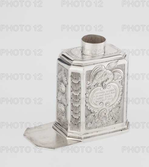 Tea caddy by Nash, Bowles fl. 1720–ca. 1725, goldsmith; rococo style. Cuboid tea caddy with a circular domed lid and a bowl on top; chamfered side edges; movable slide-in bottom. Surface decorated with repoussé ornament of floral and rocaille motifs on a grained background; front has an oval rocaille cartouche topped with an eagle, with engraved inscription inside: KENNETH Mc LEOD, / to his much loved Sister / ANNE ZABA, / Oct 23rd 1848; back wall with a bouquet of flowers; sides with blooming, leafy roses. Engraved S on the bottom; tins dated 1723/1724; decoration dated ca. mid-19th century. Origin: London, England, Great Britain. Material: vessel for loose-leaf tea; height 12 cm, width 7.7 cm, depth 5.7 cm, weight ca. 230 g., A metallic container with a reflective silver surface, shown resting on a flat silver base that extends outward; the container has an octagonal shape with a wide cylindrical opening at the top and ornate raised decorative panels on its sides featuring embossed s...